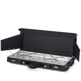 A black portable folding camp stove with two burners, shown open on a clean white background. The stove features a black metal body with silver stainless steel burner grates and control knobs.